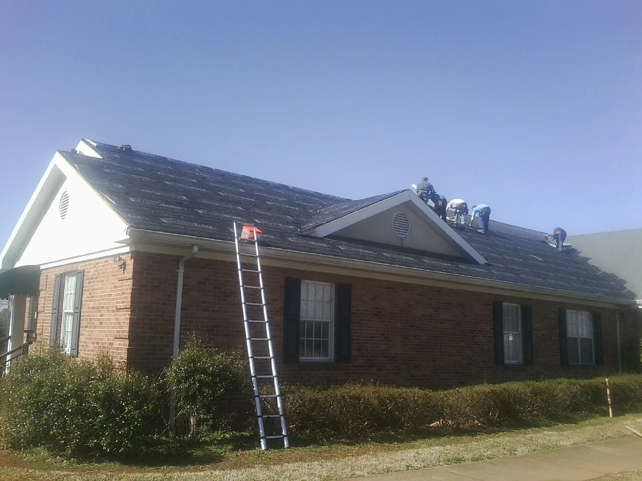 Crew tearing shingles off a brick ranch roof with a ladder set — Emergency Roof Repair work by our crew in White
