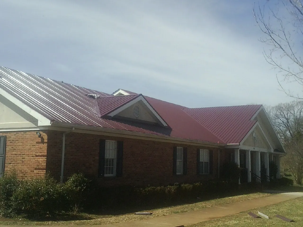 Red metal roof with gabled entries on a long brick building, from a Hail Damage Roof Repair job in White