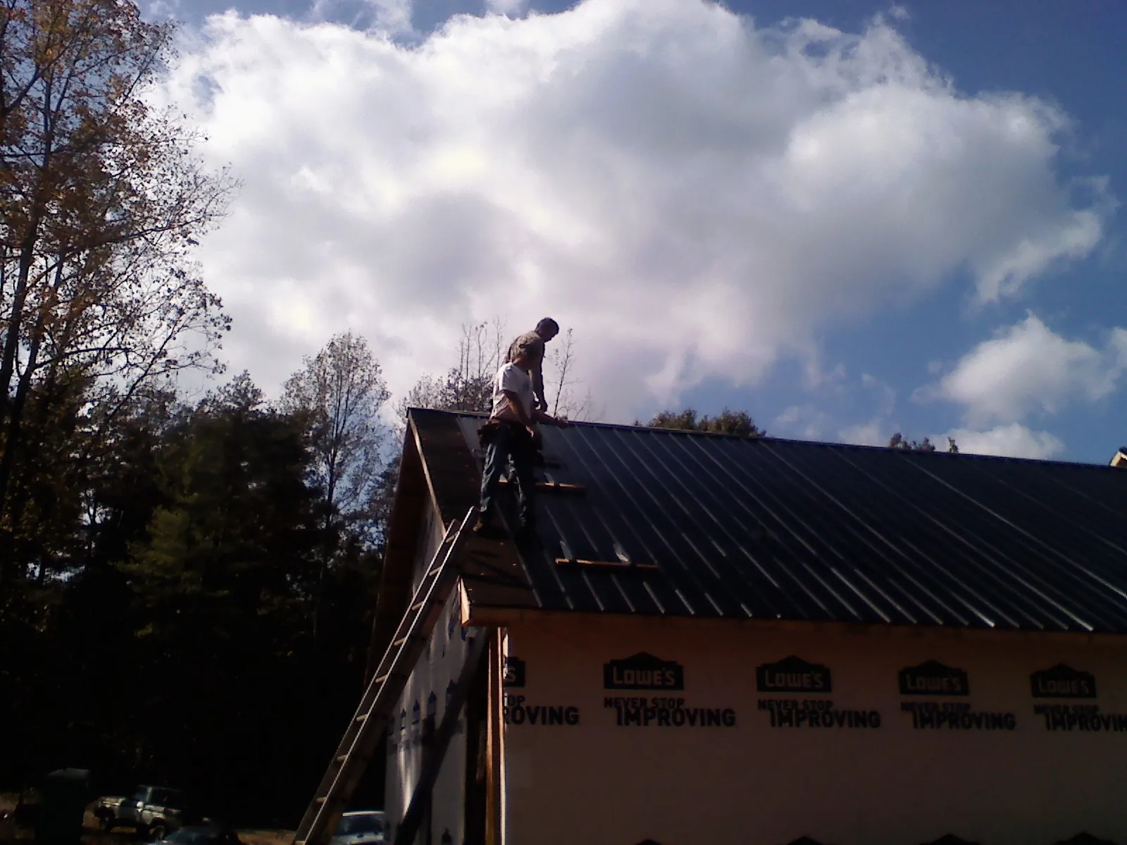 Roofer fastening dark metal panels high against a cloudy sky, from a Roof Inspection job in White