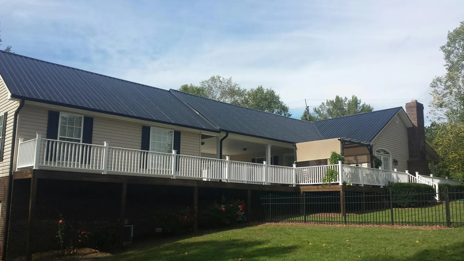 Black metal roof above a long white railed deck on a hillside home in White